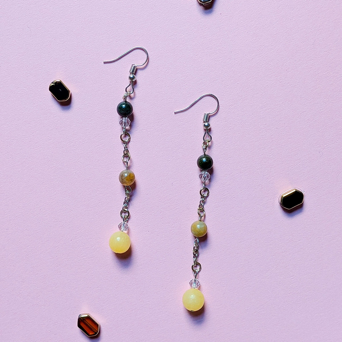 UniquelyYou handcrafted drop earrings with yellow and forest green beads on silver-tone chains against a pink background