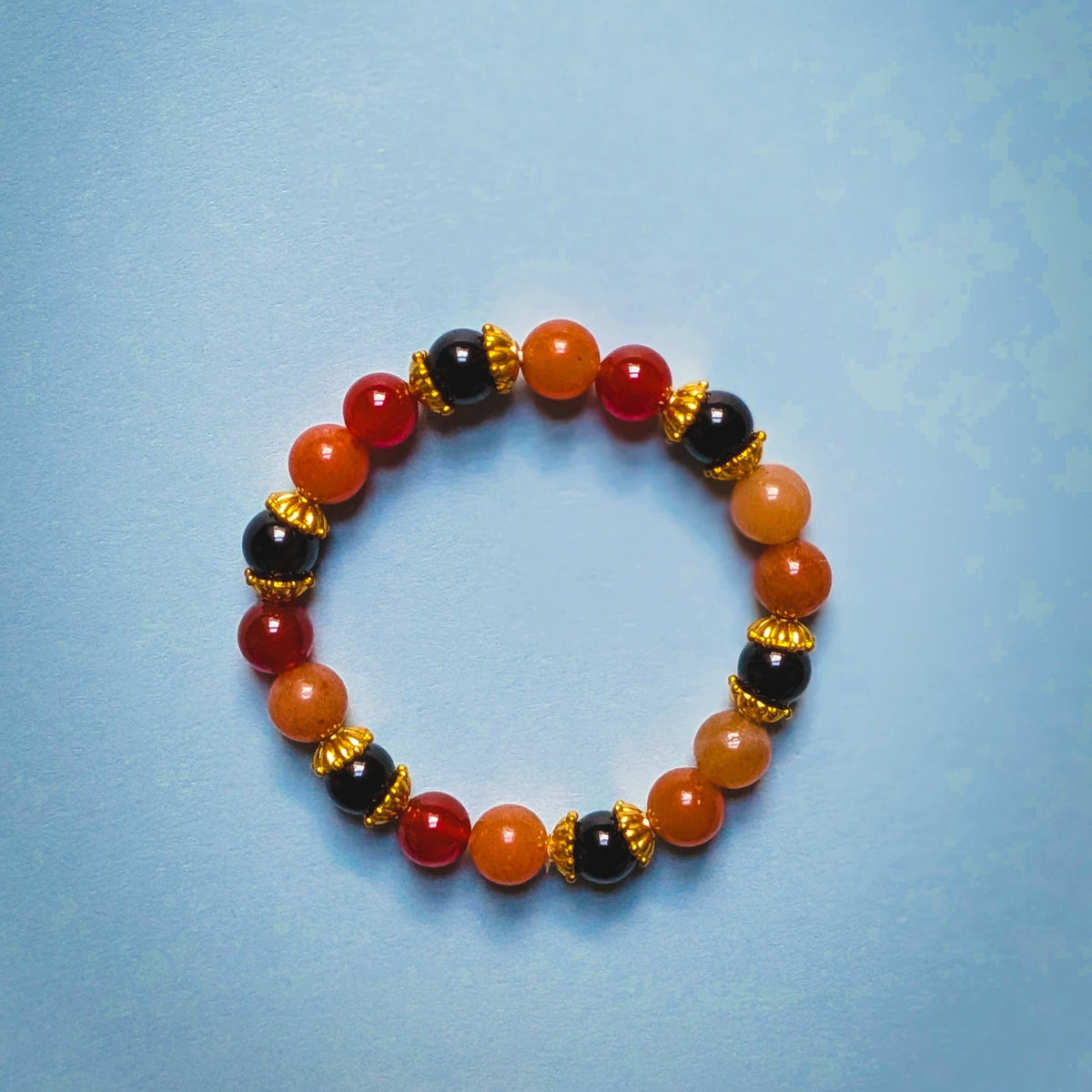 UniquelyYou stretch bracelet featuring red, orange, and black gemstone beads with intricate gold-tone metal spacers.