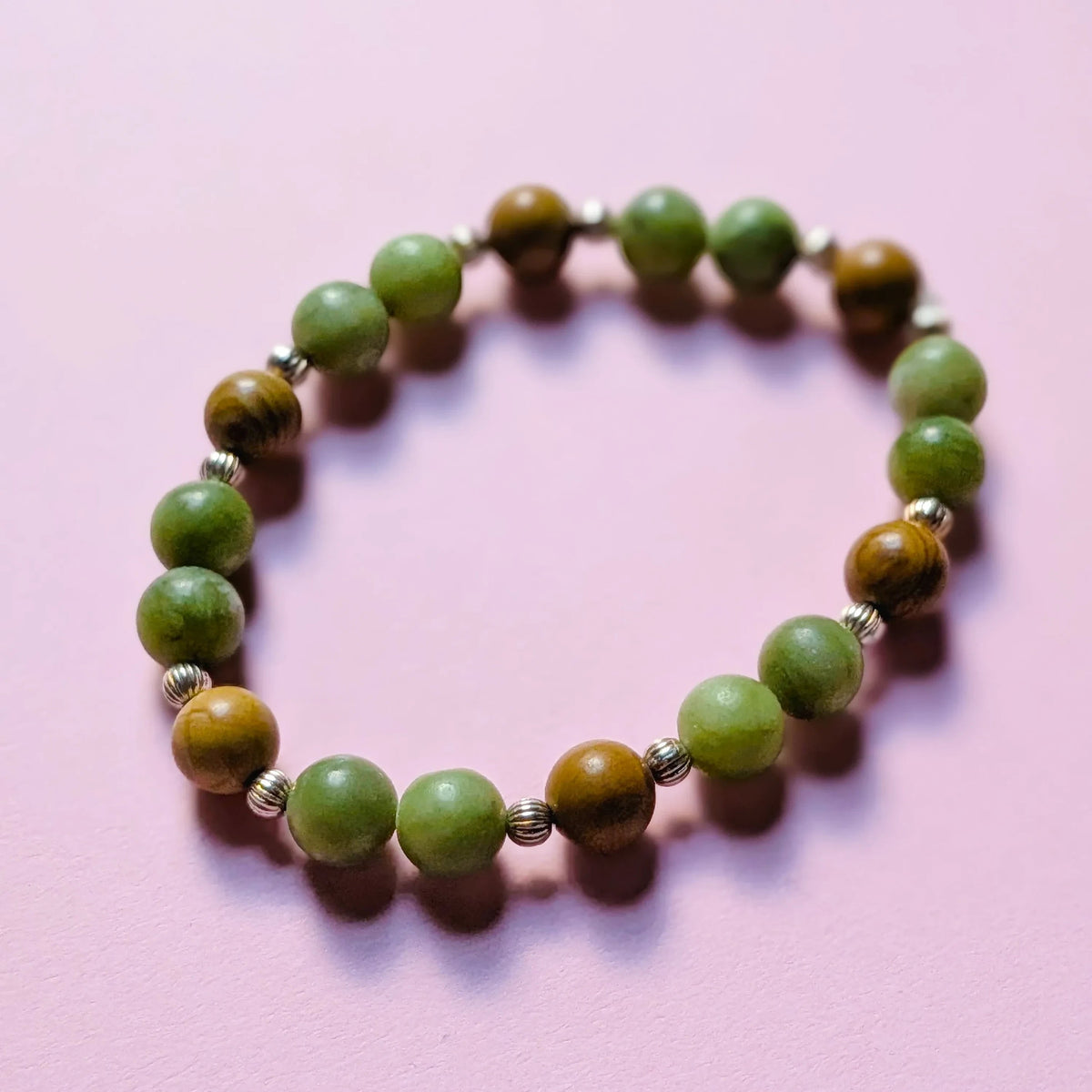 UniquelyYou stretch bracelet featuring green stone and brown wood beads with silver-tone spacers on a pink background.
